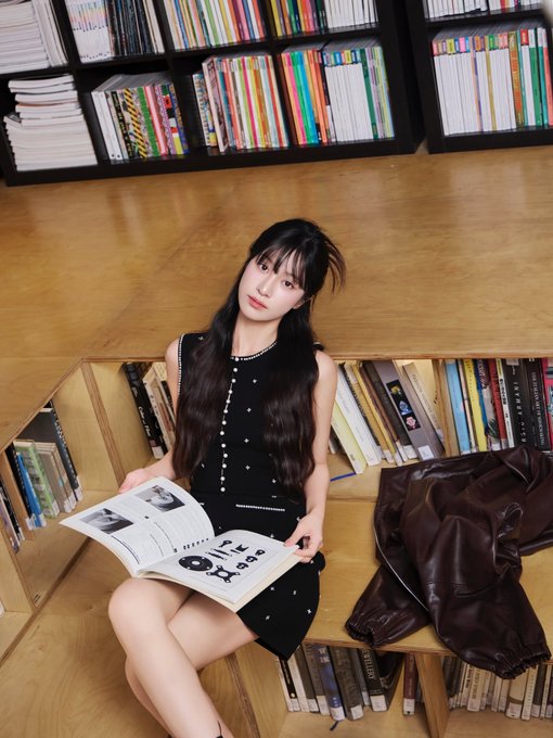 An AI-generated photo of a young woman in a black sleeveless dress sits on a wooden bench surrounded by bookshelves, holding an open book with text that includes 'in the'.