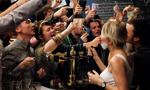 A lively bar scene where a crowd of patrons is reaching out with money to a bartender, with another woman being kissed by a man in the foreground.