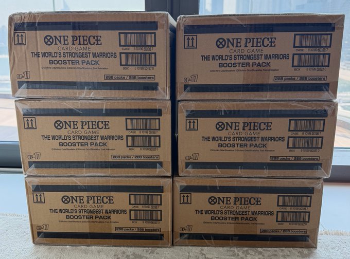 Six sealed cases of One Piece Card Game "The World's Strongest Warriors" Booster Pack (OP17) are stacked near a window, ready to be ripped open for the release day.