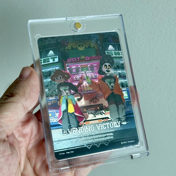 A hand holds a clear plastic card holder displaying a colorful trading card titled 'VENDING VICTORY' featuring two stylized characters in front of a vending machine, with 'Elliot, Kun_Tao' printed at the bottom.