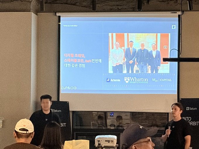 A presentation slide displayed on a screen shows a photo of four men with logos for 'Wharton Community Ventures', '4 Artemis', and 'M31 CAPITAL', with Korean text including '디지털 크레딧' on the left.