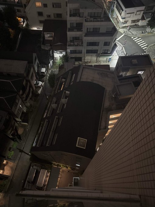 A nighttime aerial view of a narrow urban alleyway with traditional and modern buildings. The downward perspective over rooftops and a street lit by ambient lights evokes a sense of departure, fittingly matching the post's farewell "bye."