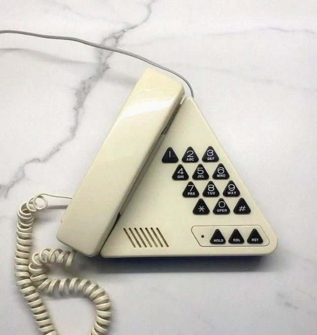 A vintage cream-colored triangular push-button telephone with a coiled cord rests on a white marble surface.