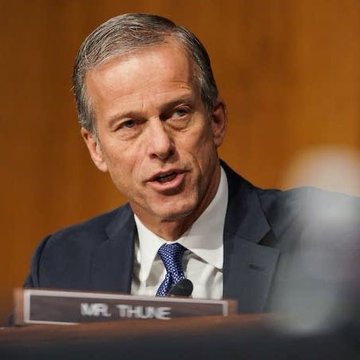 Senator John Thune speaks during a hearing, identified by the "MR. THUNE" nameplate in front of him, as the post notes his role in delaying the CLARITY Act amid CR-related procedural issues and ethics concerns.