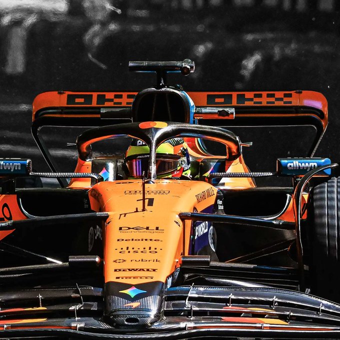 A McLaren Formula 1 race car, sponsored by Dell Technologies, Deloitte, Cisco, Rubrik, and DeWalt, speeds down a track with its driver visible inside the cockpit halo. The bold orange livery and dynamic front-on angle capture the high-speed intensity of the sport, aligning with the post's message about Belgium launching a new era.