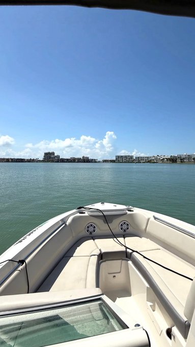 A view from the bow of a boat cruising across turquoise waters toward a coastal city skyline under a bright blue sky, fitting the playful "Happy Mutant Monday" countdown vibe as a scenic lead-up to the 61-day mark until ApeFest.