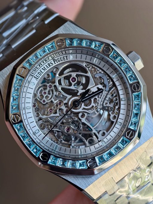 A close-up of a luxury Audemars Piguet Royal Oak watch with a skeleton dial, baguette-cut blue topaz bezel, and stainless steel bracelet.