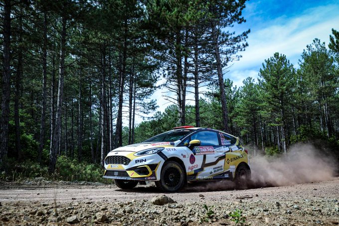 A Binance-branded rally car, featuring "PIN" sponsorship, races through a dusty pine forest stage during the ESOK Eskişehir Rally on September 18-20. The caption highlights driver Kübra Denizci Keskin and co-driver Kerem Deveci securing the women's category win and a third-place finish in the RC5 class, with Binance TR's support.