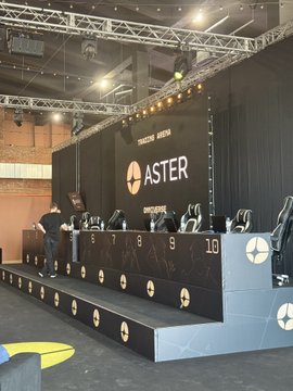 An esports gaming setup featuring the ASTER token by Superform, with a stage, gaming chairs numbered 6, 9, and 10, and an "ASTER" logo on the backdrop screen.