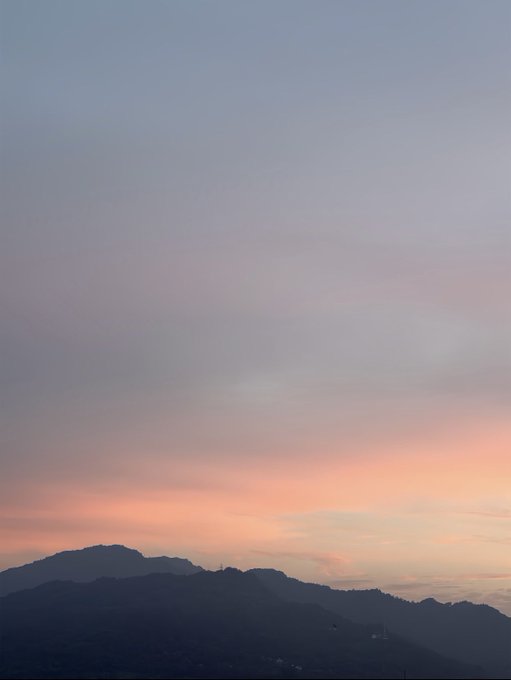 A serene view of mountain silhouettes against a soft pastel sunset sky transitioning from blue at the top to orange and pink near the horizon.