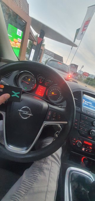 A first-person view from inside an Opel car shows a hand holding a black credit card with a green "X" logo, waiting in a drive-thru lane with a McDonald's menu board visible outside. The image ties into the post by featuring xPortal (the X-branded MultiversX wallet) at a McDonald's drive-thru, framing it as the "perfect combo" of fast food and crypto.