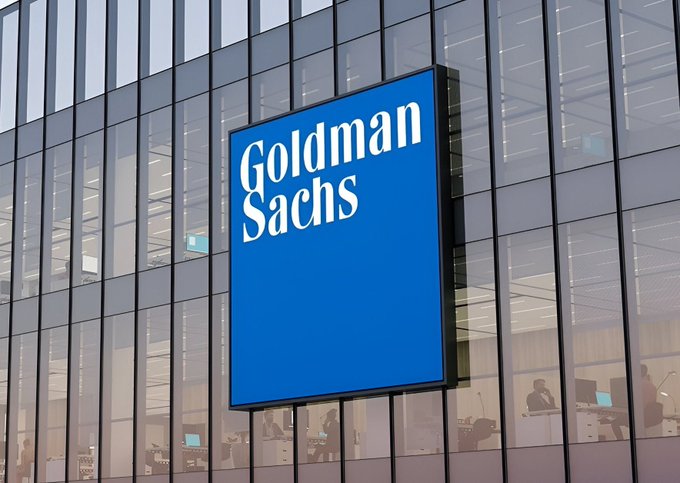 A Goldman Sachs sign is displayed on the exterior of a glass office building, with employees visible working at their desks inside, illustrating the bank's prominent presence in the financial sector.

The image connects to the post by showing the Goldman Sachs headquarters, the company whose CEO has publicly called for the U.S. to pass the crypto market structure bill to establish regulatory clarity for digital assets.
