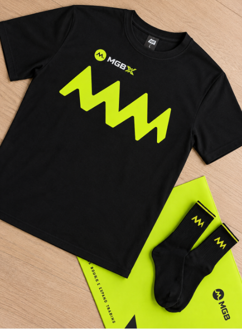 A black MGBX branded t-shirt with a neon green logo laid out next to matching socks on a wooden surface.