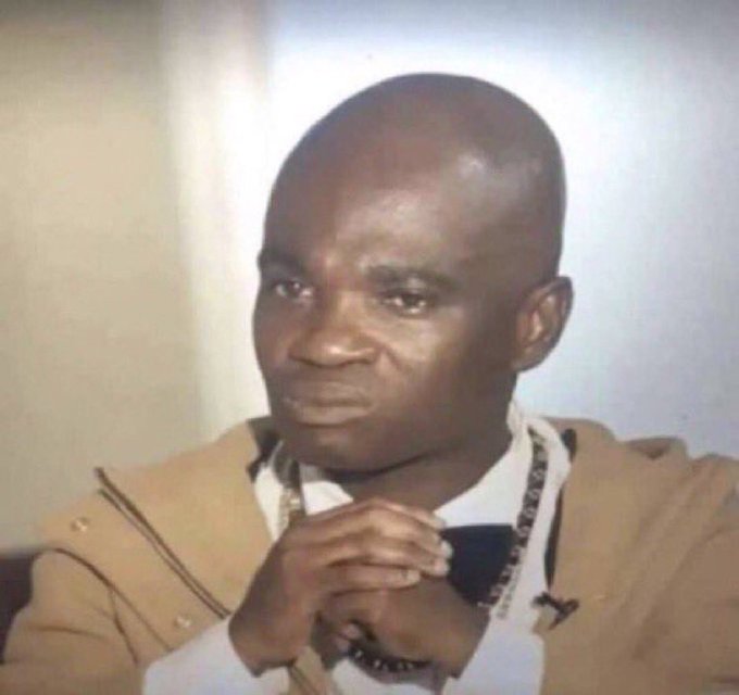 A screenshot of a man in a tan jacket with his hands clasped together, appearing to be in a moment of prayer or contemplation.