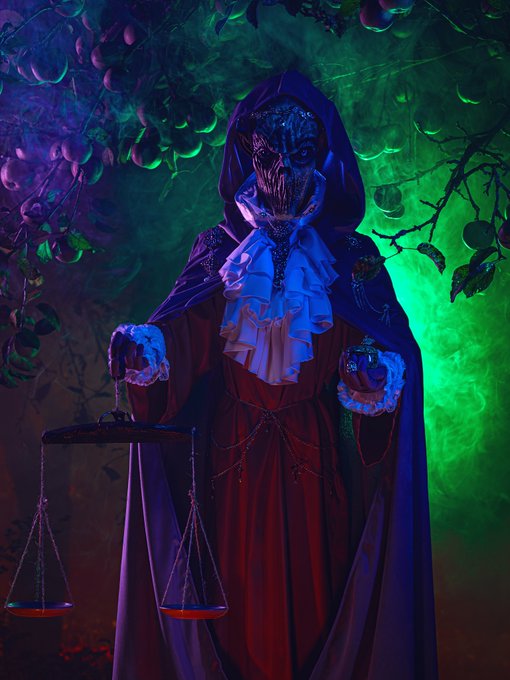 A mysterious figure in a red robe and skull mask holds a scale, illuminated by dramatic purple and green lighting.