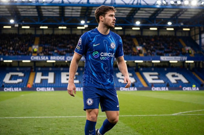 A Chelsea football player wearing a blue home kit with 'Circle USDC' sponsor logo walks on the pitch at Stamford Bridge stadium.