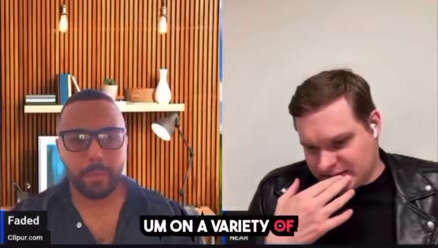 The image shows a man wearing glasses sitting next to another person, who appears to be a male actor or someone with a beard. They are both looking at each other across a computer screen, which has a caption that reads "Um on a variety of AI history". The background features a wooden wall and a shelf filled with various items such as books and vases.