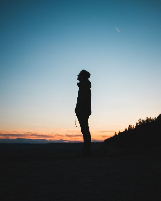 A silhouetted figure stands alone against a vibrant sunset sky as a shooting star streaks overhead, embodying the optimistic spirit of "New Day, New Opportunities."