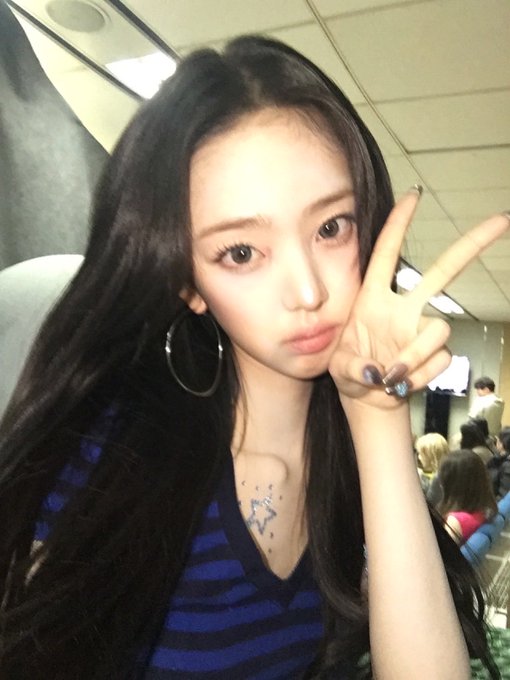 A young woman with long dark hair, wearing large hoop earrings and a blue striped top, posing with a peace sign near her face.