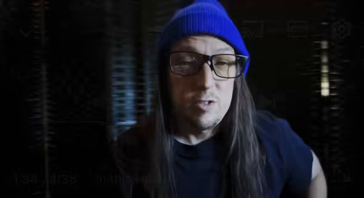 The image features a man wearing glasses, a blue beanie hat, and a black shirt with the text "Aeon @mikesemler dropped a New YouTube Video - SPX690 0 is Bitcoin 2.0". The focus of the image is on the man's face as he looks at the camera.