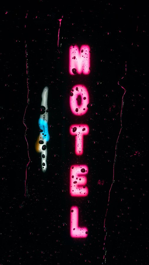 A glowing pink neon sign reading 'MOTEL' with water droplets on it, accompanied by a smaller blue light on a dark background.