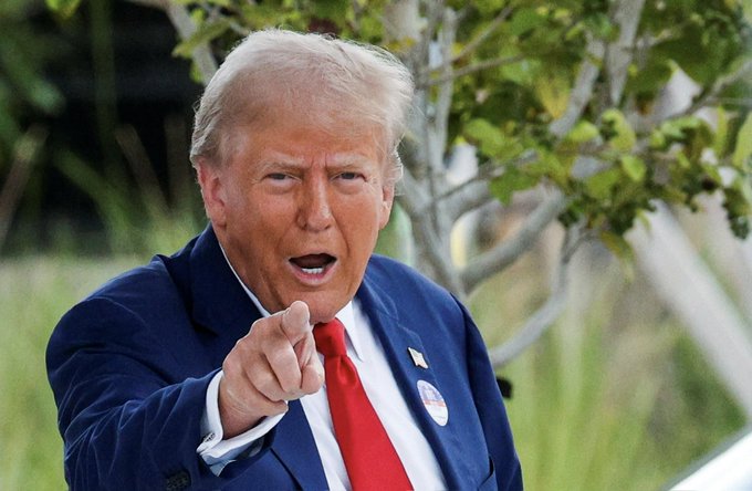 A man in a dark blue suit and red tie points directly at the camera with an open-mouthed expression, appearing mid-speech, with what looks like a small badge on his lapel. The accompanying post references a "Trump Insider" trading account making bold calls on cryptocurrencies like $ZEC and $BTC, implying a connection to this public figure who projects an air of confident, insider authority.