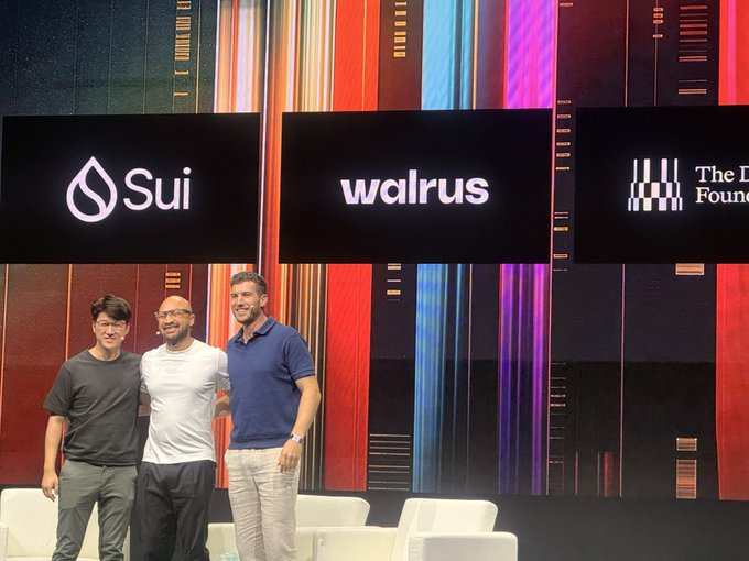 Three men standing on a stage with logos for Sui, Walrus, and what appears to be The [something] Foundation displayed on screens behind them.