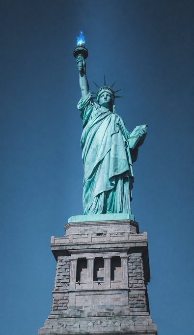 The Statue of Liberty stands tall against a deep blue sky, holding her iconic torch aloft, symbolizing the principles of freedom and self-sovereignty that align with the post's message about cryptocurrency's role in giving individuals direct control over their finances.