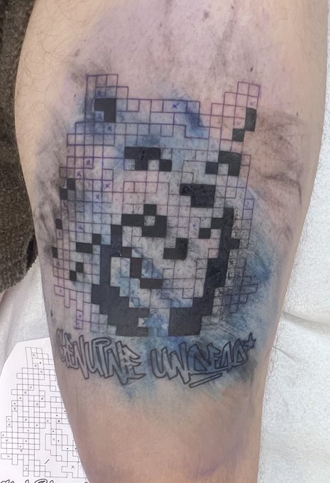 A healed leg tattoo featuring a QR code design in black ink with a watercolor-style blue and purple background. Below the QR code reads "@GENUINELY UNDEAD" in graffiti-style lettering, matching the tagged artist @GenuinelyUndead mentioned in the post.