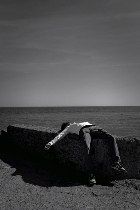 A person in dress pants and a white shirt lies sprawled motionless on a stone seawall, suggesting exhaustion. The image visually echoes the post's theme of burnout, illustrating the need for rest rather than more tracking or productivity tools.
