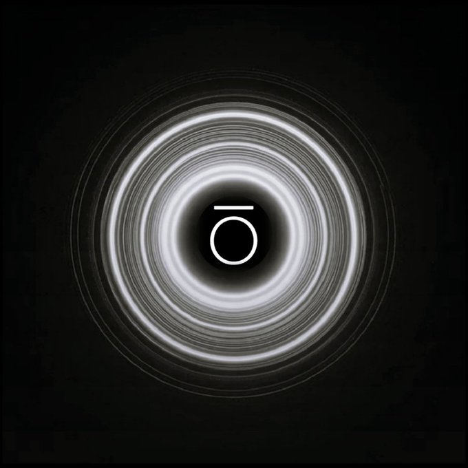 A minimalist dark image featuring concentric white circular light rings around a small central symbol resembling a camera or stopwatch icon.