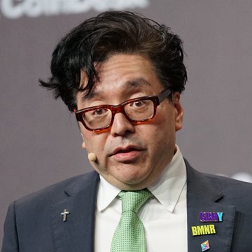 A man wearing glasses, a dark suit, and a green tie speaks at a podium, displaying a "BMNR" pin (BitMine Immersion's ticker) on his lapel, connecting to the post about the company's massive $ETH unrealized losses.