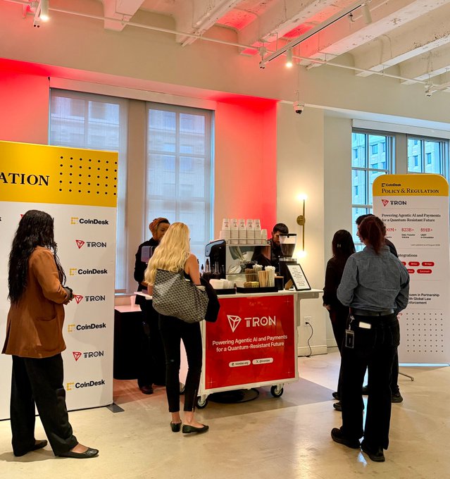 People gather around a coffee cart branded with the 'TRON' logo at what appears to be a CoinDesk and TRON event, with promotional banners visible.