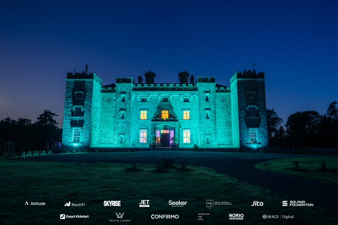 A castle illuminated in teal and purple lights at night, with sponsor logos displayed along the bottom including Altitude, SKYROSE, JET, Seeker, Jito, and others.