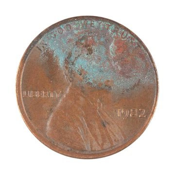 A close-up of a heavily corroded 1982 Lincoln penny with green oxidation spots and visible 'IN GOD WE TRUST', 'LIBERTY', and '1982' markings.