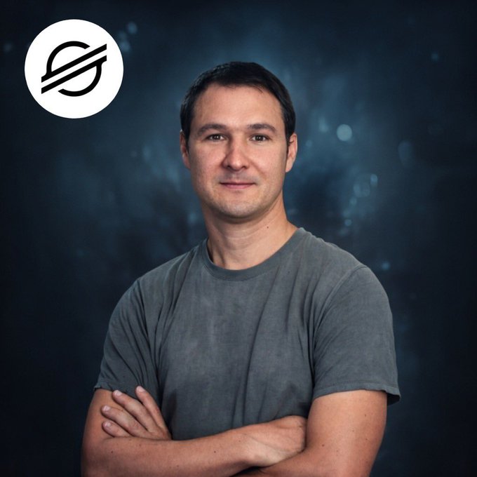 A professional portrait of a man with short dark hair wearing a gray t-shirt with his arms crossed, set against a dark blue textured background with the Stellar (XLM) logo in the top left corner.