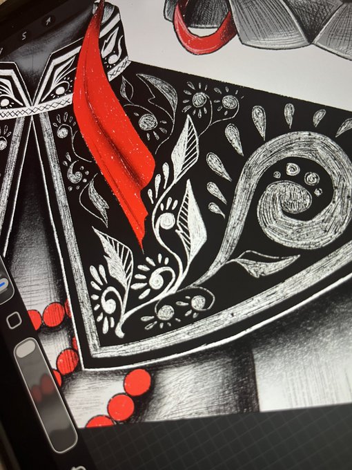 A close-up photo of an artistic illustration on a tablet, featuring a striking red feather and intricate black-and-white floral and spiral patterns.