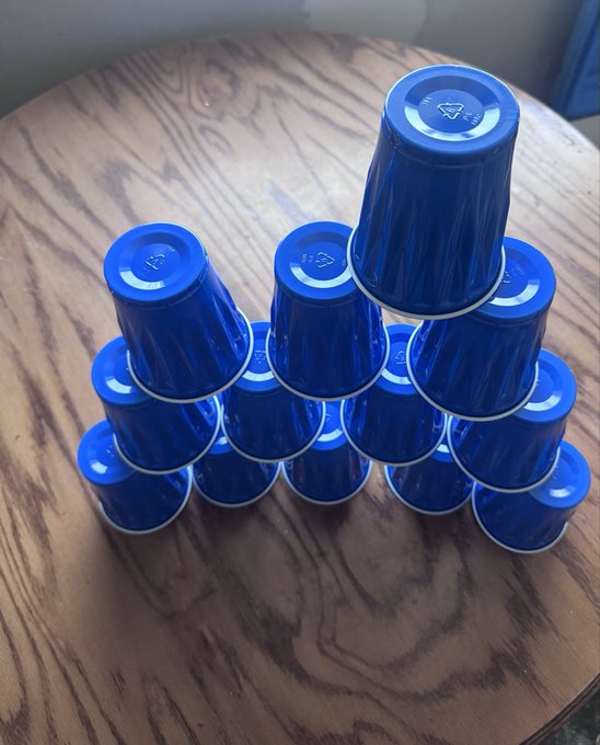 A pyramid stack of blue plastic cups with recycling symbols arranged on a round wooden table.
