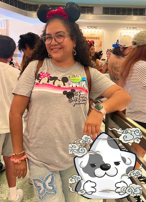 The image features a woman wearing a gray t-shirt with a cartoon dog on it, standing next to a railing at an indoor location. She has a large smile on her face as she poses for the photo. The background of the image shows other people present in the scene, but they are not the main focus of the picture. The caption provided seems to be unrelated or unrelated to the woman and her t-shirt with the cartoon dog.