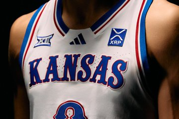 The image shows a close-up of a Kansas Jayhawks basketball uniform featuring the team's signature "KANSAS" wordmark in blue lettering across the chest, along with a prominent "XRP" sponsor logo and the Big 12 conference patch, visually confirming the new Ripple partnership announced by Kansas Athletics to bring the XRP brand to Jayhawk uniforms.
