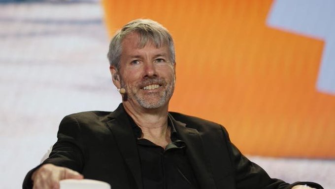 Michael Saylor, executive chairman of MicroStrategy, smiles while speaking at a conference with an orange background.