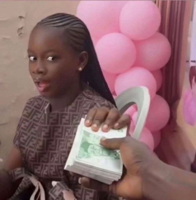 A young girl with braided hair in a brown patterned dress holds a thick stack of Nigerian naira bills, looking surprised, with pink balloons in the background.