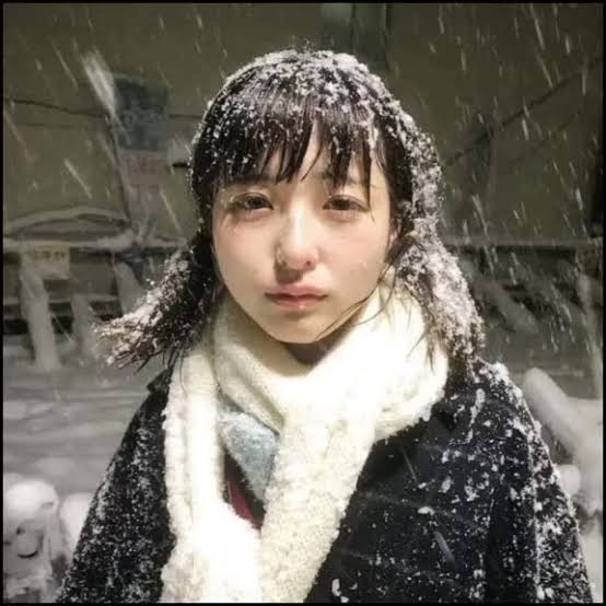 A young woman stands in falling snow, her hair and dark coat dusted with snowflakes, wearing a white scarf and looking directly at the camera with a somber, resigned expression. The icy, melancholic atmosphere of the image mirrors the post's feeling of being stranded and "tokenless" after a failed coffee date, capturing the cold disappointment of a solo moment.

No text, numbers, or addresses are visibly legible in the image itself.