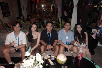 A group of five young adults sitting together on a couch posing for a photo at what appears to be an evening social event.