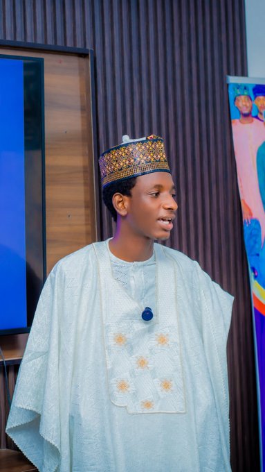 A young man wearing a traditional embroidered cap and white ceremonial attire stands in a modern indoor setting with colorful artwork in the background, appearing to be the trader or mentor referenced in the post. The image visually represents the "chief" or mentor figure (@YahayaCrypto) being honored for his role in shaping a successful trading journey, aligning with the post's tribute to those who guide others in crypto trading.