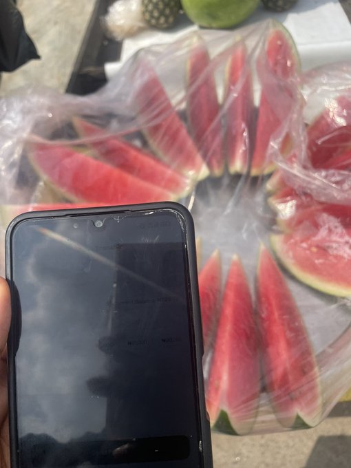The image shows a person holding a cell phone with a screen displaying an advertisement for Spenda, a mobile banking app. The text on the phone reads "it's about a 100 degrees in Lagos good thing I have the Spenda app! i got fruit on my way back home aboki asked me which bank I used i will onboard him soon download the Spenda app!". This post seems to be promoting the use of Spenda as an alternative banking option for people who are interested in mobile payments and accessing financial services through their smartphones.