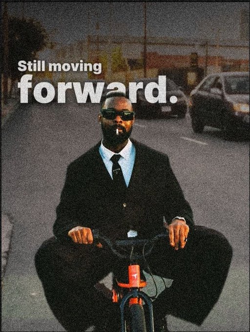 A stylishly edited photo of a man in a black suit and sunglasses riding a red bicycle down a street, overlaid with the text 'Still moving forward.'
