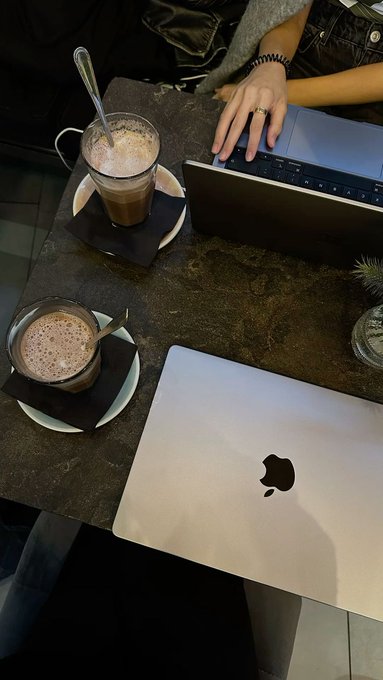 An overhead view of a coffee shop table with two MacBook laptops and two glasses of chocolate beverages.