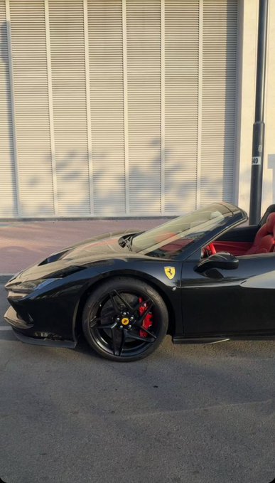 A sleek black Ferrari convertible with red brake calipers and red leather interior gleams under sunlight, parked against a metal shutter building. The image embodies the post's message of a confident, flashy "Good Morning" flex—showcasing luxury and status as an undeniable response to doubters.