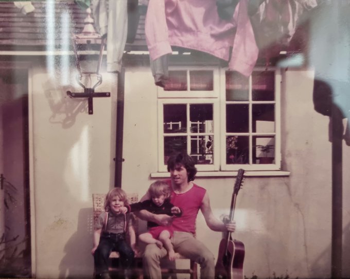 A vintage family photo shows a man in a red sleeveless shirt with two young children in front of a house, with what appears to be a Bored Ape Yacht Club (BAYC) NFT image overlaid at the top, matching the post's reflection on how the man's red shirt coincidentally resembles the iconic red BAYC shirt from 42 years ago.